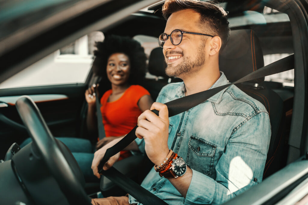 young-multiracial-couple sitting in a-car-and-fastening-seat-belts-road-safety
